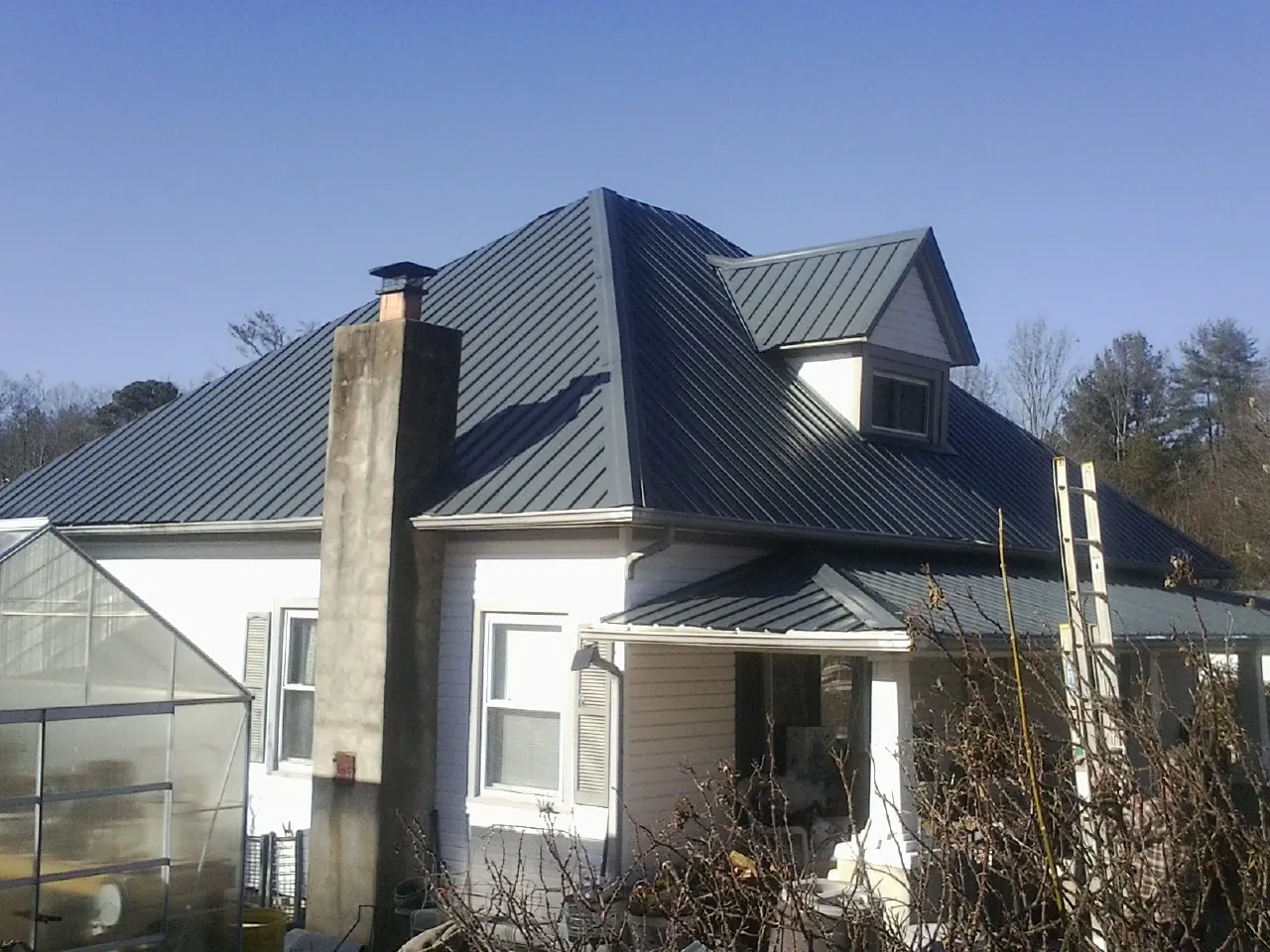 Dark blue standing seam metal roof on a white farmhouse with dormer — Slate & Tile Roof Repair by Roofing Brothers in Wellington